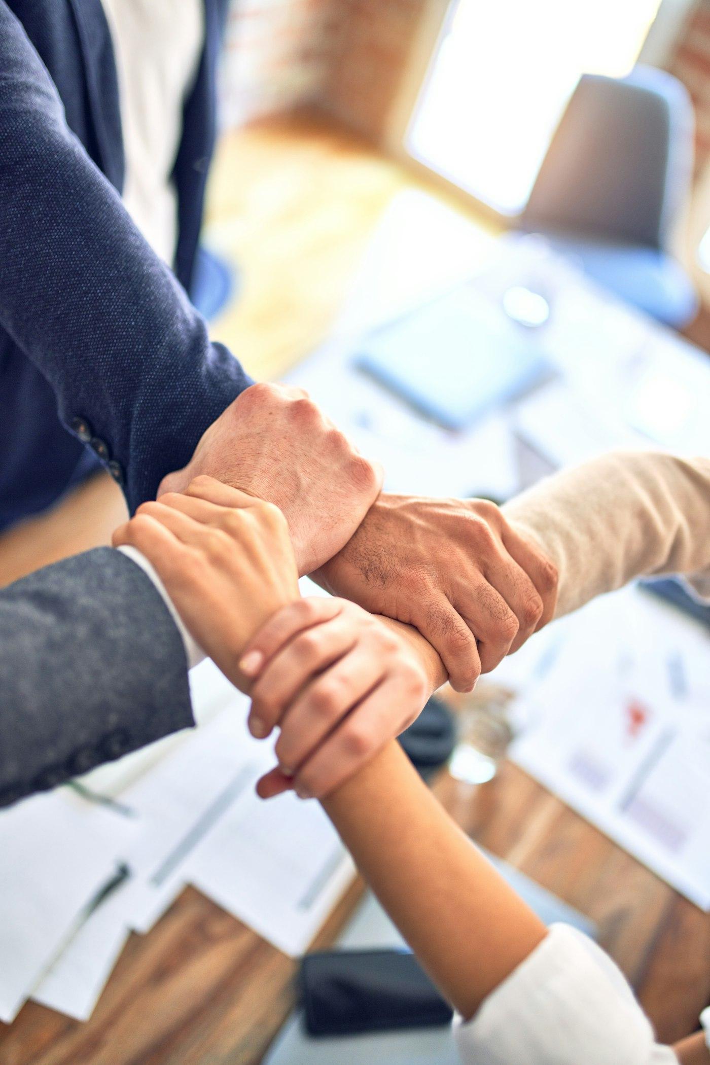 A tight-knit advisory team joining hands over a strategy table